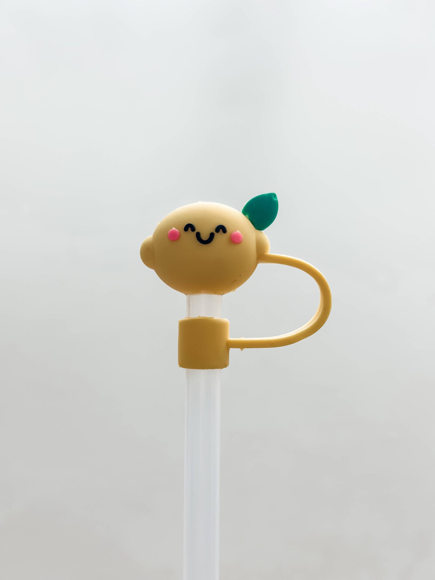 Silicone straw cover shaped like a smiling yellow lemon with pink cheeks, green leaf, and handle. Fits standard straws. Sizes: standard.