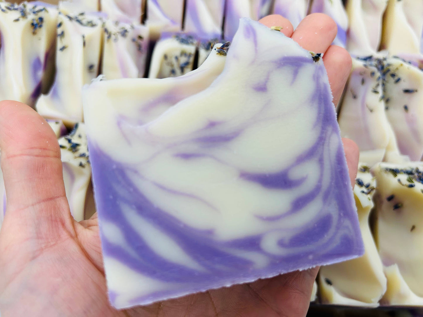 This Vegan Cold Process Handmade Soap Bar boasts a marbled lavender and white design. The soap has a gentle lavender fragrance, enhanced by the dried lavender buds sprinkled on the top edge, creating an appealing aesthetic touch. This soap is cruelty-free and vegan-friendly. Available in one standard size.