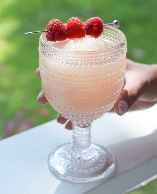 Textured glass of light pink Frosé Ready to Freeze Slush Mix, garnished with raspberries. Available in 4oz, 8oz, and 16oz sizes.