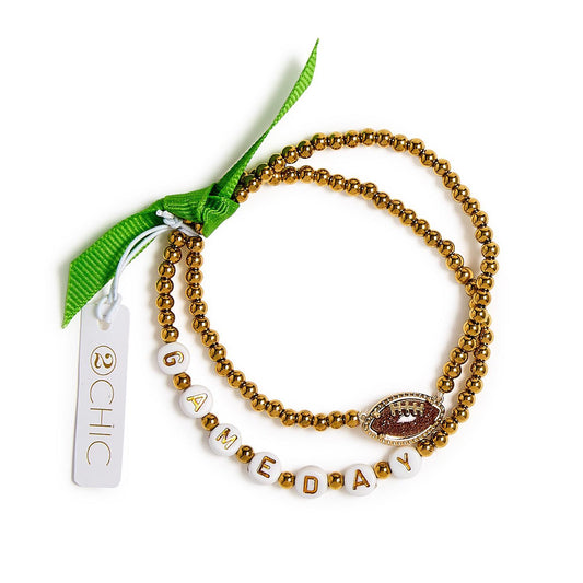 Game Day Stretch Bracelet Set includes two gold beaded stretch bracelets: one with white beads spelling "GAMEDAY" and a football charm, the other with a green ribbon and CHIC tag. Available in one size.