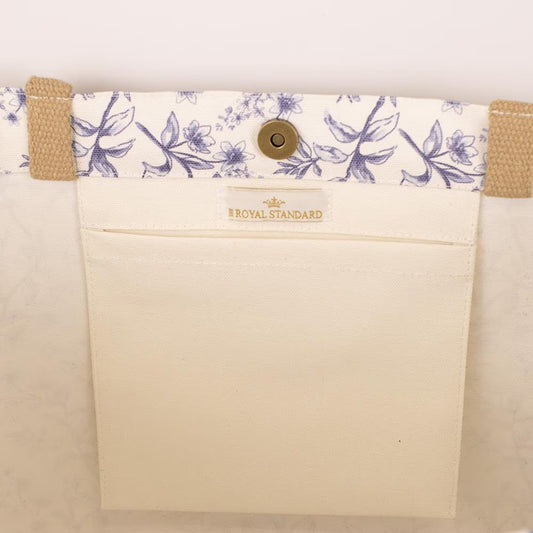 The Aldridge Garden Classic Tote offers a spacious interior with a blue and white floral-patterned inner border. It features two brown woven handles and a snap closure. Size: One size available.