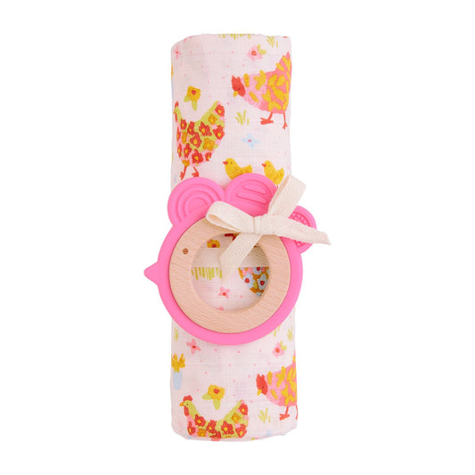 A Pink Farm Swaddle & Teether Set rolled up and tied with a bow, featuring a pink teething ring attached to it. The blanket is decorated with tiny animal prints.