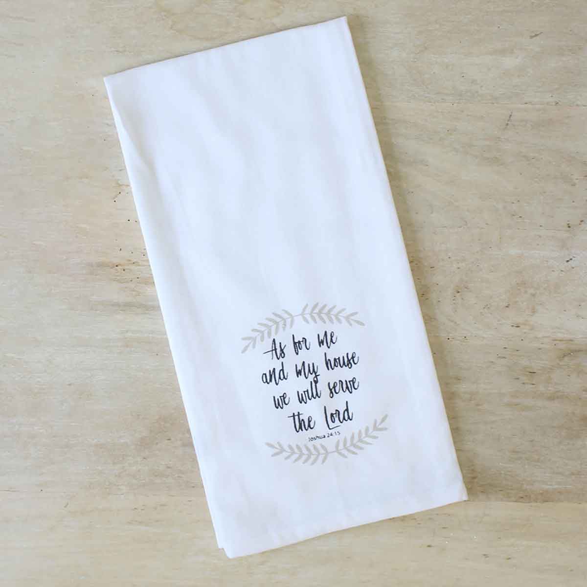 White cotton Joshua 24:15 hand towel with decorative script and leafy wreath. Available in standard size. Machine wash cold.