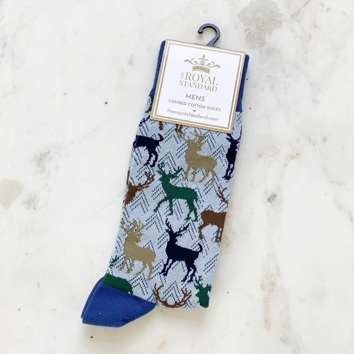 The Royal Standard's Men's Stag Socks feature a blue base with a multicolored deer pattern on a light, marbled background. Available sizes: Medium, Large.