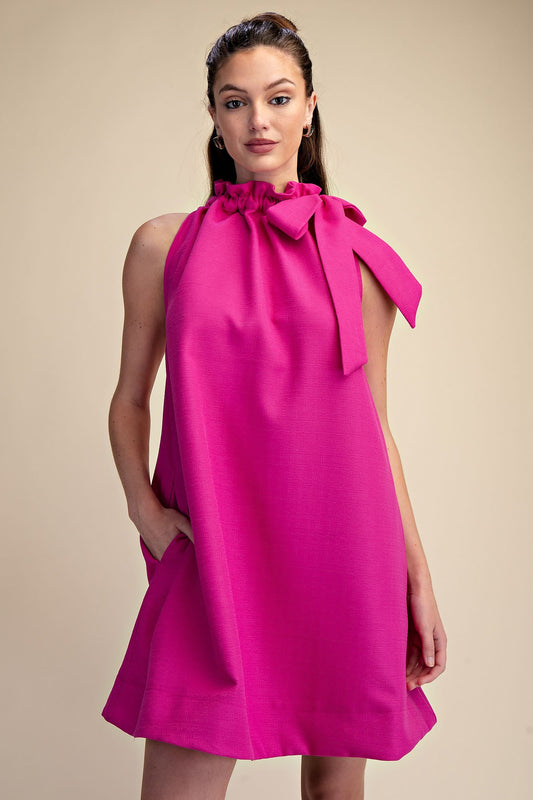 Magenta Tie-Neck Sleeveless Dress with high neckline, shoulder bow, and ruffle detail. Available in sizes XS-XL.
