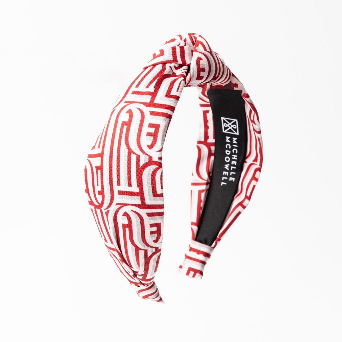 The Luna Touchdown Headband is a red and white geometric design accessory with a stylish top-knot, featuring a black inner lining. Available in one size fits most.