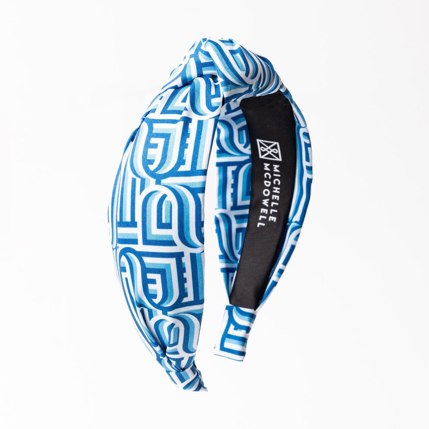 The Luna Touchdown Headband features a blue and white geometric pattern with a top-knot design. Available in one size.