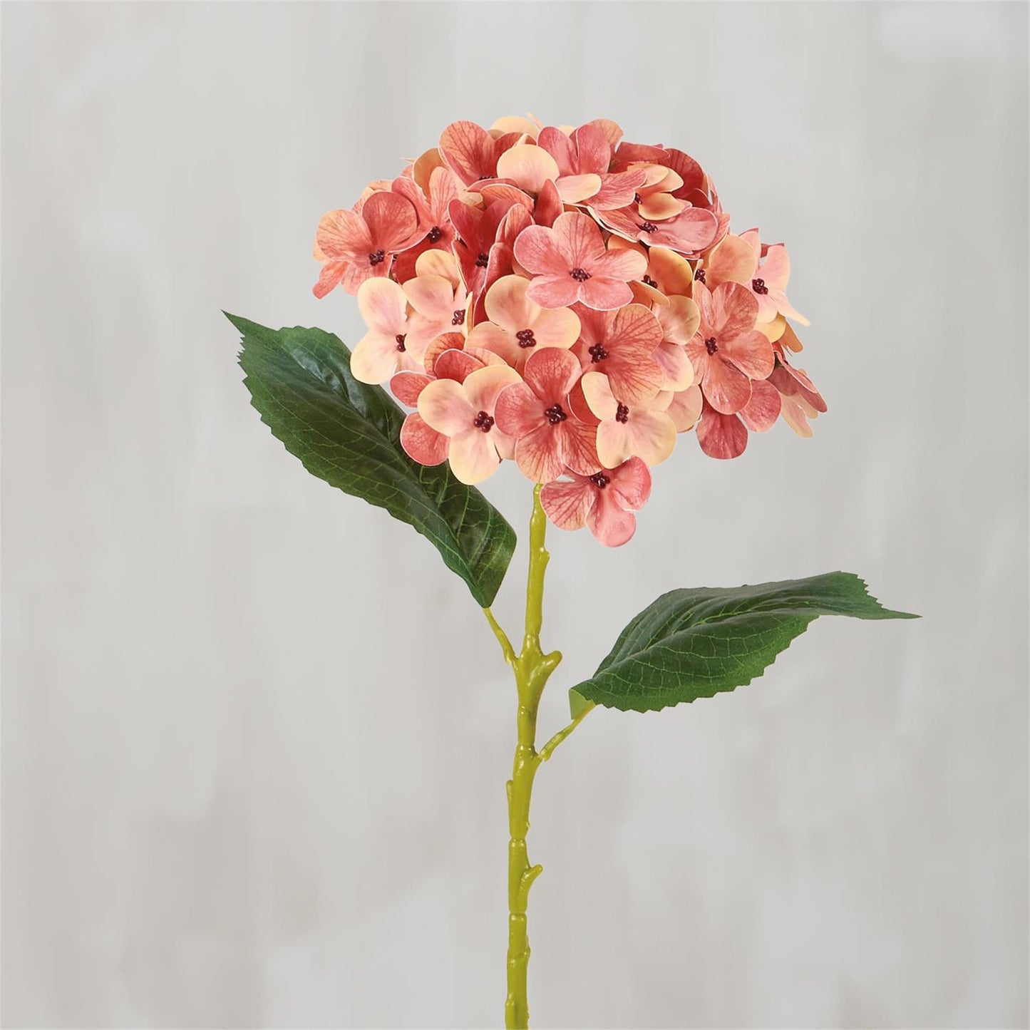 The Pink Hydrangea Floral Pick is an artificial stem with orange and pink hydrangea flowers and two large green leaves. Available size: one standard stem size.