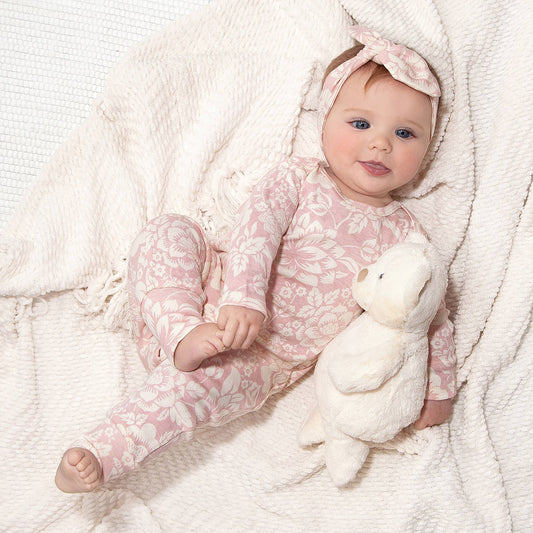 Baby modeling romper with matching headband (sold seperately). Baby is holding bear with one arm and foot with hand laying down.