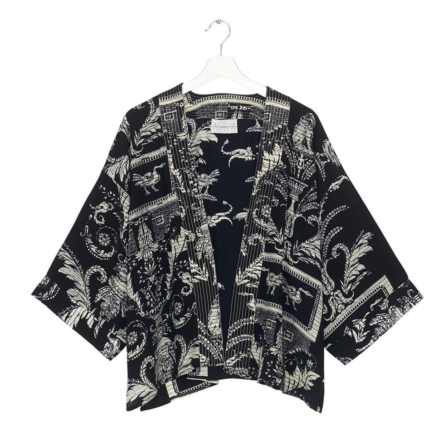 The Vintage Damask Black Short Kimono is made from crepe fabric with intricate white patterns of tropical leaves and decorative swirls. Available in sizes S, M, L, and XL.