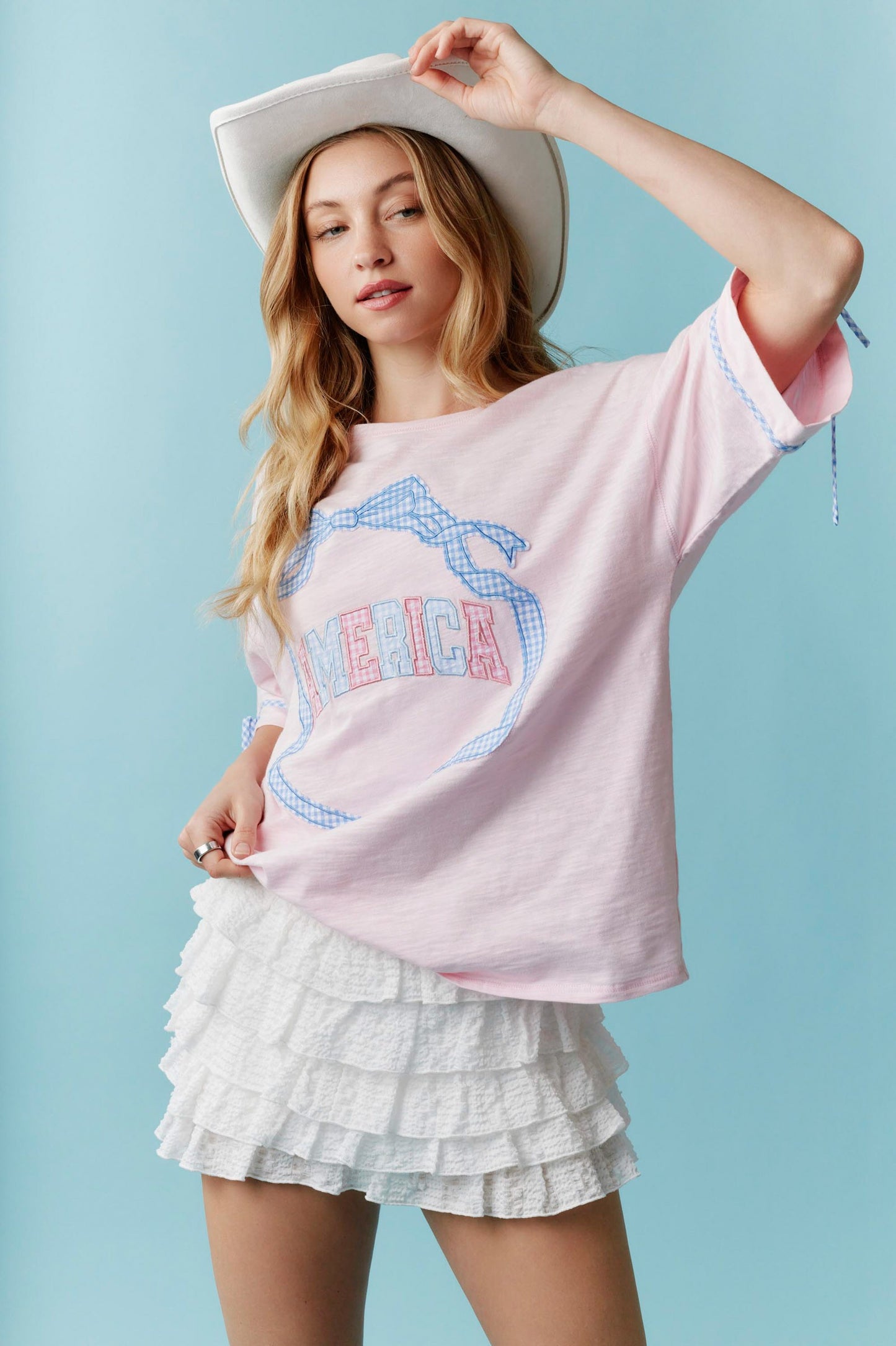 Americana Gingham Bow T-Shirt: White tee with blue trim and red gingham bow detail. Available in sizes XS–XL.