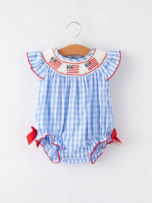 Blue and white gingham girls romper with flag smocking, red trim, red bows. Sizes: 2T-6T.