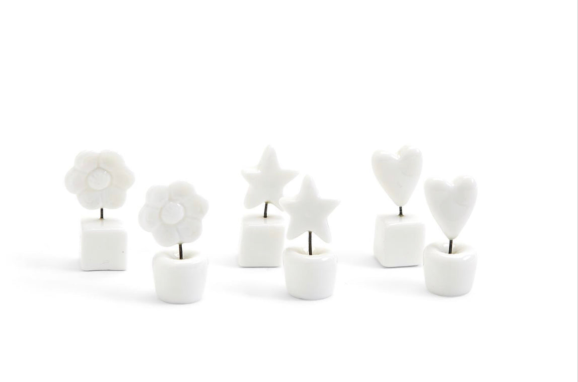 Six small white ceramic holders with metal stems topped by white flowers, stars, or hearts; available in one compact size.