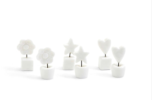 Six small white ceramic holders with metal stems topped by white flowers, stars, or hearts; available in one compact size.