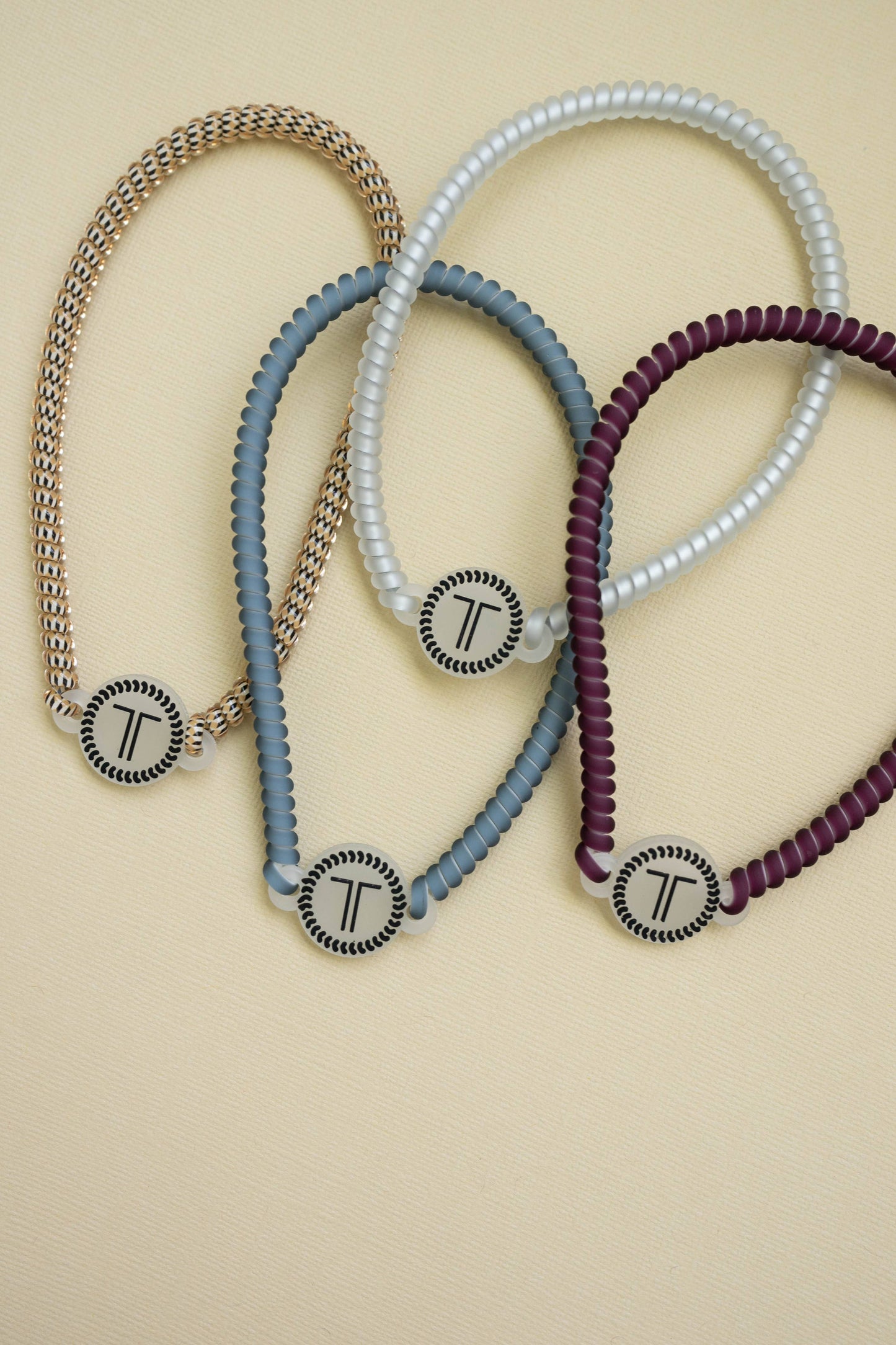 TELETIES Spiral Hair Coil Headband set of four, colors: gold, blue-gray, white, burgundy with “T” charms. Sizes: small/large.