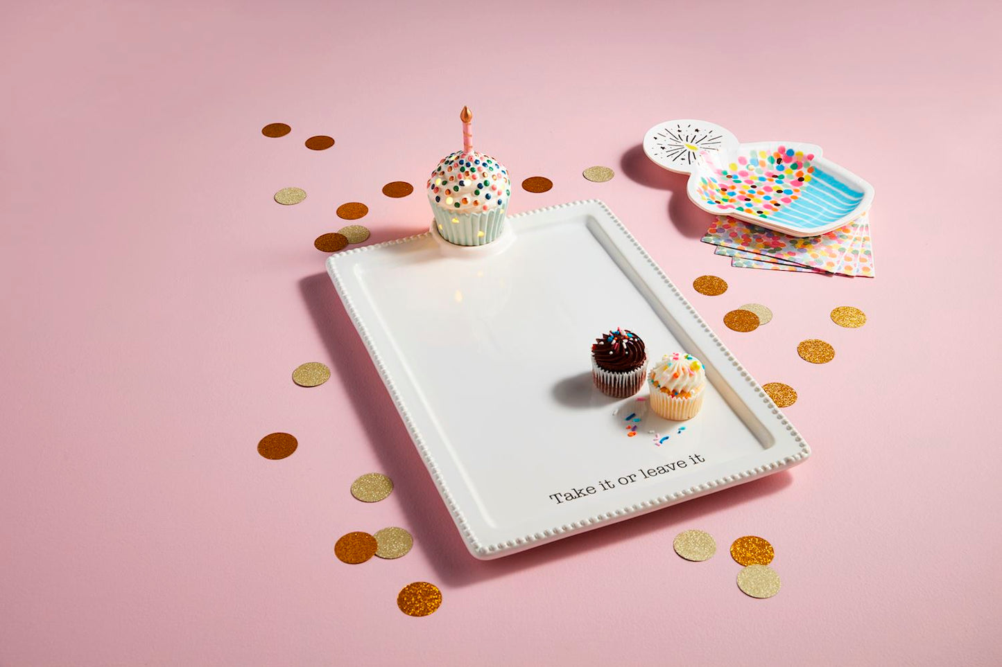 The Cupcake Light-Up Sitter features a hand-painted white rectangular plate with the phrase "Take it or leave it" on the edge. It holds three sprinkle-adorned cupcakes each with a candle. Sizes: Not specified.