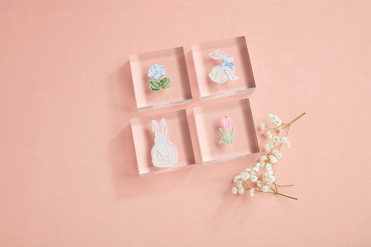 The Spring Acrylic Block set includes four clear blocks showcasing hand-painted acrylic art: a vibrant flower, a rabbit with a blue bow, another rabbit, and a tulip. Sizes available: Standard.