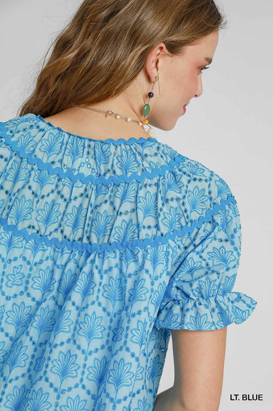 Celeste Eyelet Mini Dress in light blue with blue floral embroidery and ruffled sleeves. Available in XS–XL.