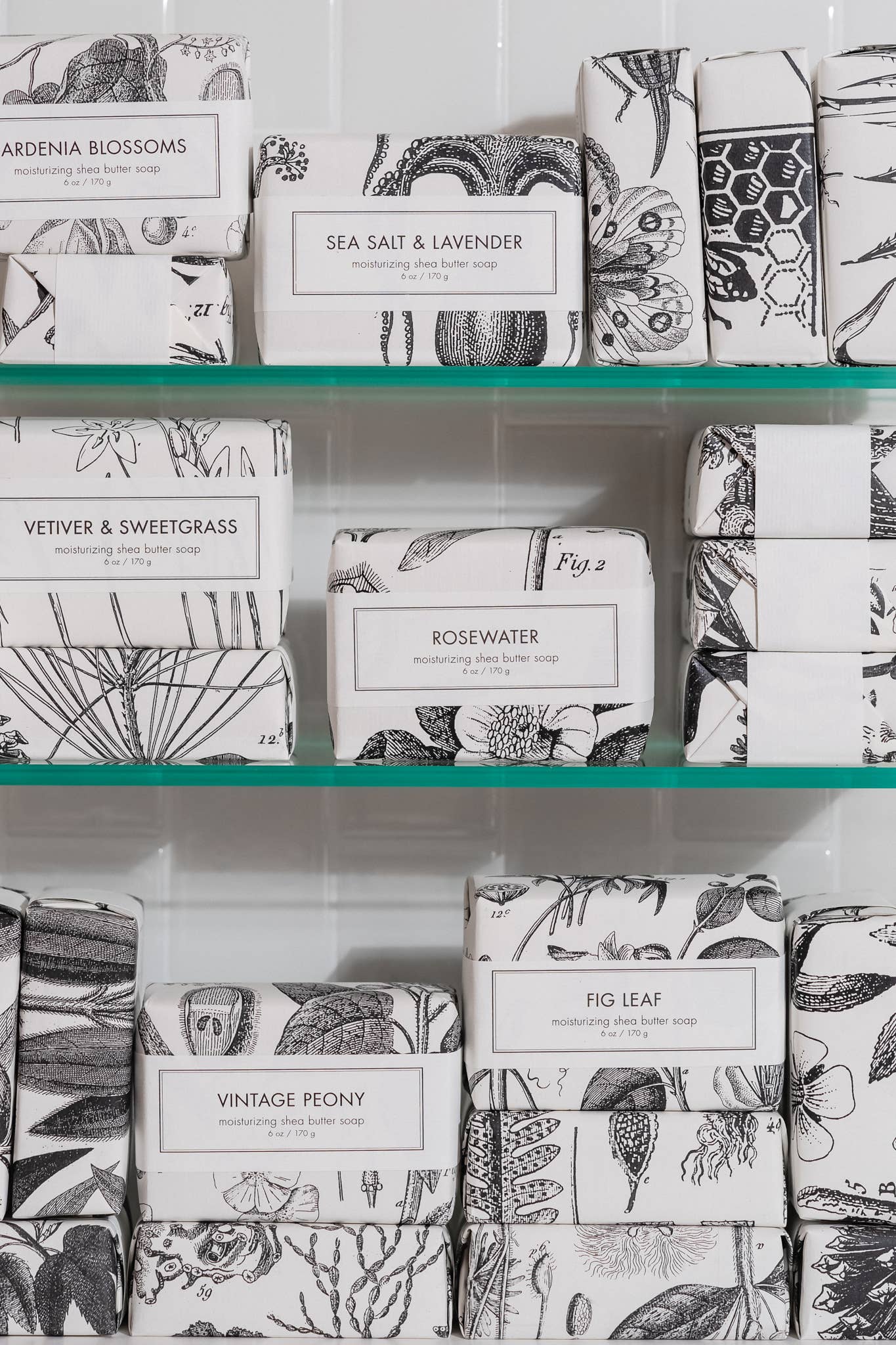 The product is Shea Butter Soap and Bourbon & Vanilla Soap - Bath Bar, beautifully packaged with labels indicating various scents. Scents include Gardenia Blossoms, Sea Salt & Lavender, and Fig Leaf. The size of the product is not specified.