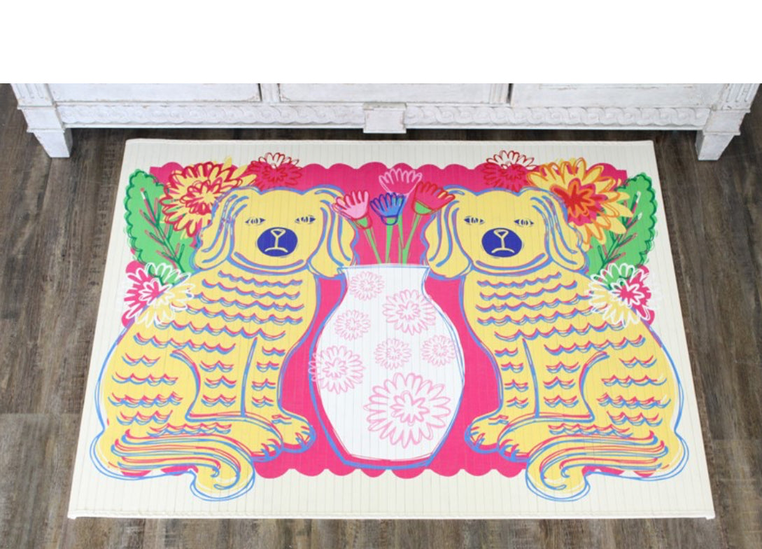 Pink, green, white flowers background with two yellow and blue Staffordshire dogs facing each other and a white vase in the middle.