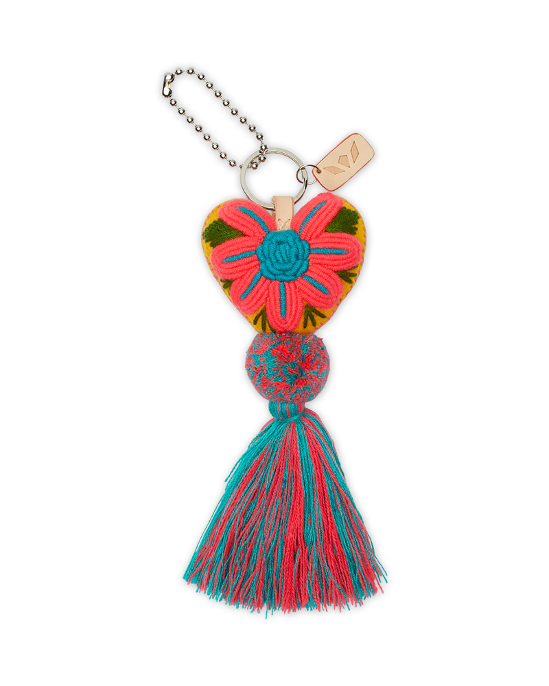 The Consuela Conni Charm keyring features a pink and green embroidered heart, blue flower, woven bead, and multicolored tassel. It includes a metal chain and tag. Size: One size available.