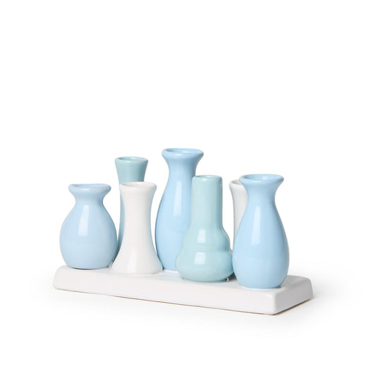 The Blue Hues Multi Vase features seven handcrafted porcelain vases in white and light blue shades, arranged on a rectangular white base. Sizes: Various sizes within the set.