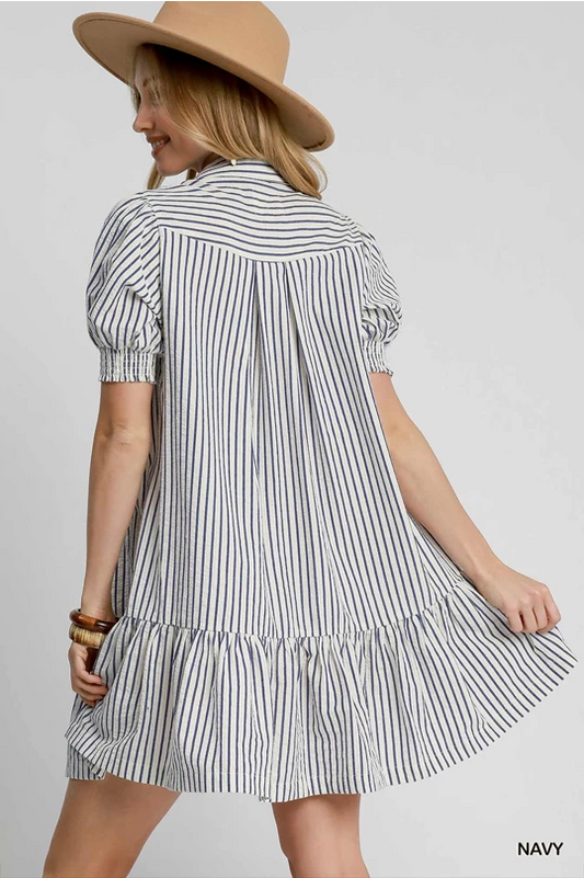 Margot Striped Dress with navy vertical stripes, short sleeves, ruffled hem, loose fit. Sizes: XS–XL.
