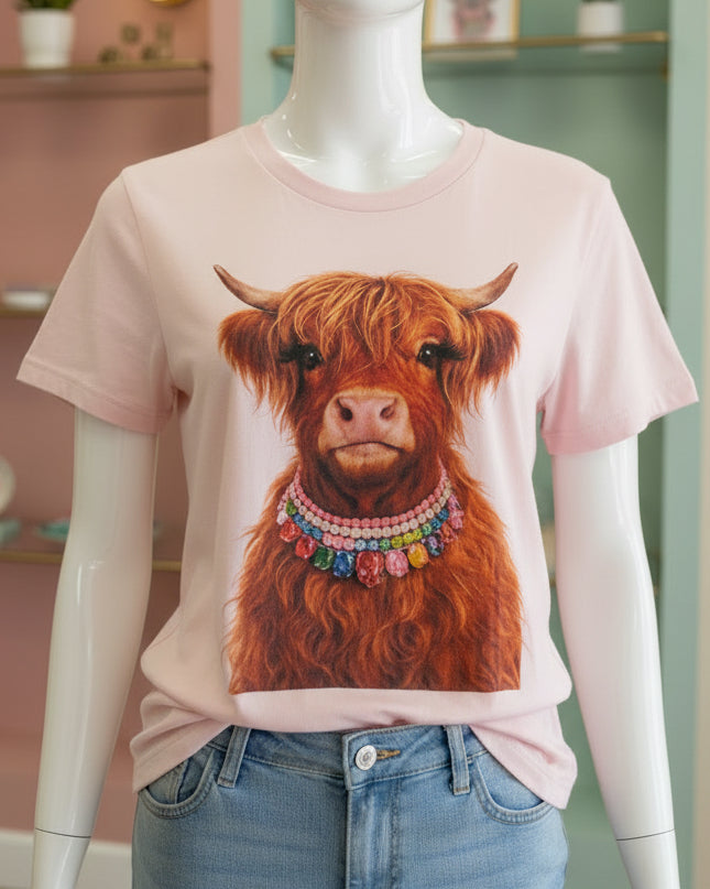 Light pink unisex Jeweled Collar Highland Calf Tee with a vibrant graphic of a Highland cow wearing colorful beaded necklaces; available in sizes S–XXL.