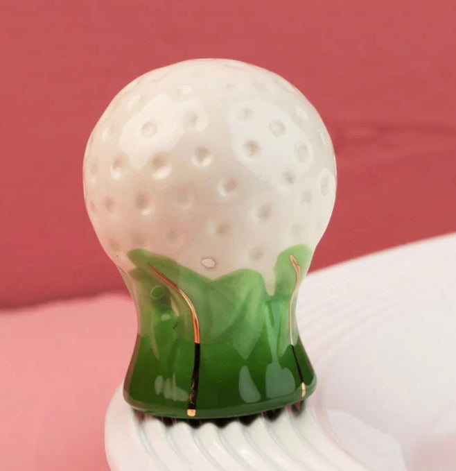 White, dimpled ceramic golf ball figurine on a green leaf base. Available in mini size.