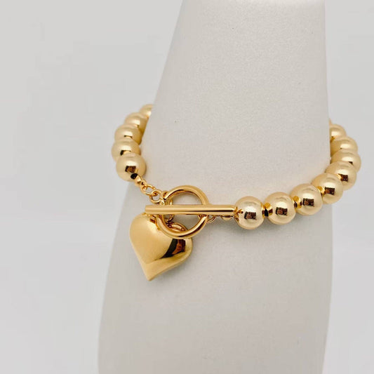 18K gold-plated bracelet with 8MM beads, heart charm, and T-bar clasp in stainless steel. Available in multiple sizes.