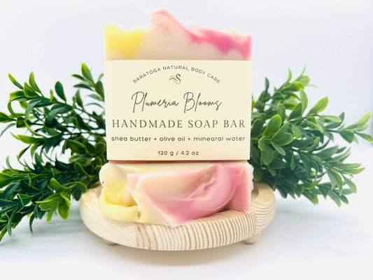 Saratoga natural body care, handmade soap bar 4.2 ounces Shea batter olive oil and mineral water. This handmade soap bars fragrance is plumeria blooms . It is moisturizing, nourishing, and gentle. It is cream with swirls of pink.