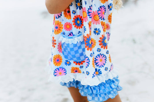 Girls Blue Check Flower Power Short Set: retro floral print, blue checkered pocket, ruffled shorts. Sizes 2T–10 available.