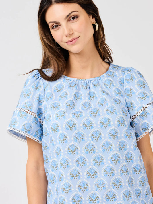 Tabby Sunshower Flora Blue Top with light blue floral pattern, flutter sleeves, and white lace trim. Sizes: XS–XL.