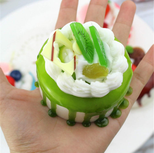 Small, round green and white faux cake with whipped cream, kiwi slices, and glossy decorative toppings. Available in multiple sizes.