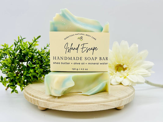 This handmade soap bar is island escape made by Saratoga natural body care. It’s made with shape better olive oil and mineral water. It’s 4.2 ounces it’s moisturizing, nursing and gentle cream edged in a light blue.
