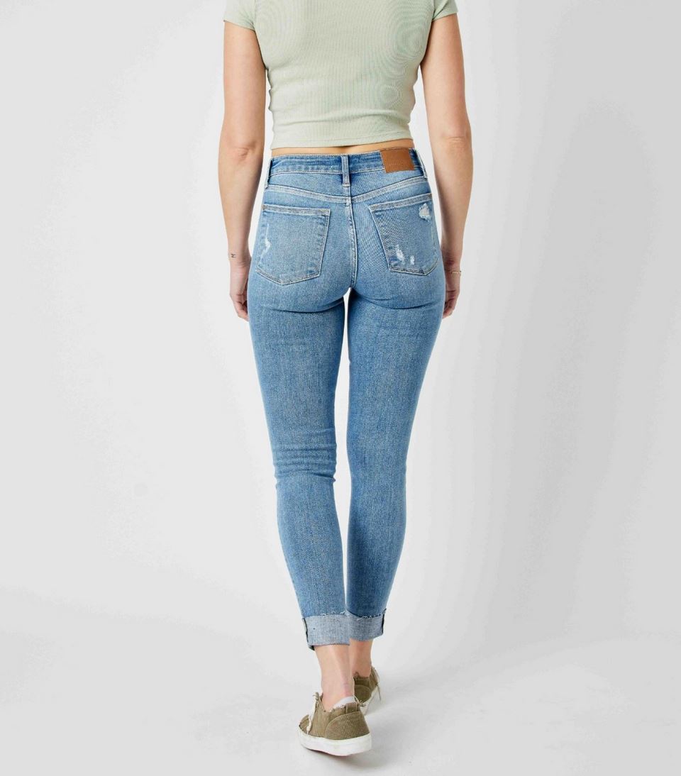 Judy Blue Mid Rise Destroy & Cuffed Skinny Jeans feature a ripped pocket, beige leather patch, and rolled-up ankles. Sizes: 0-24W.