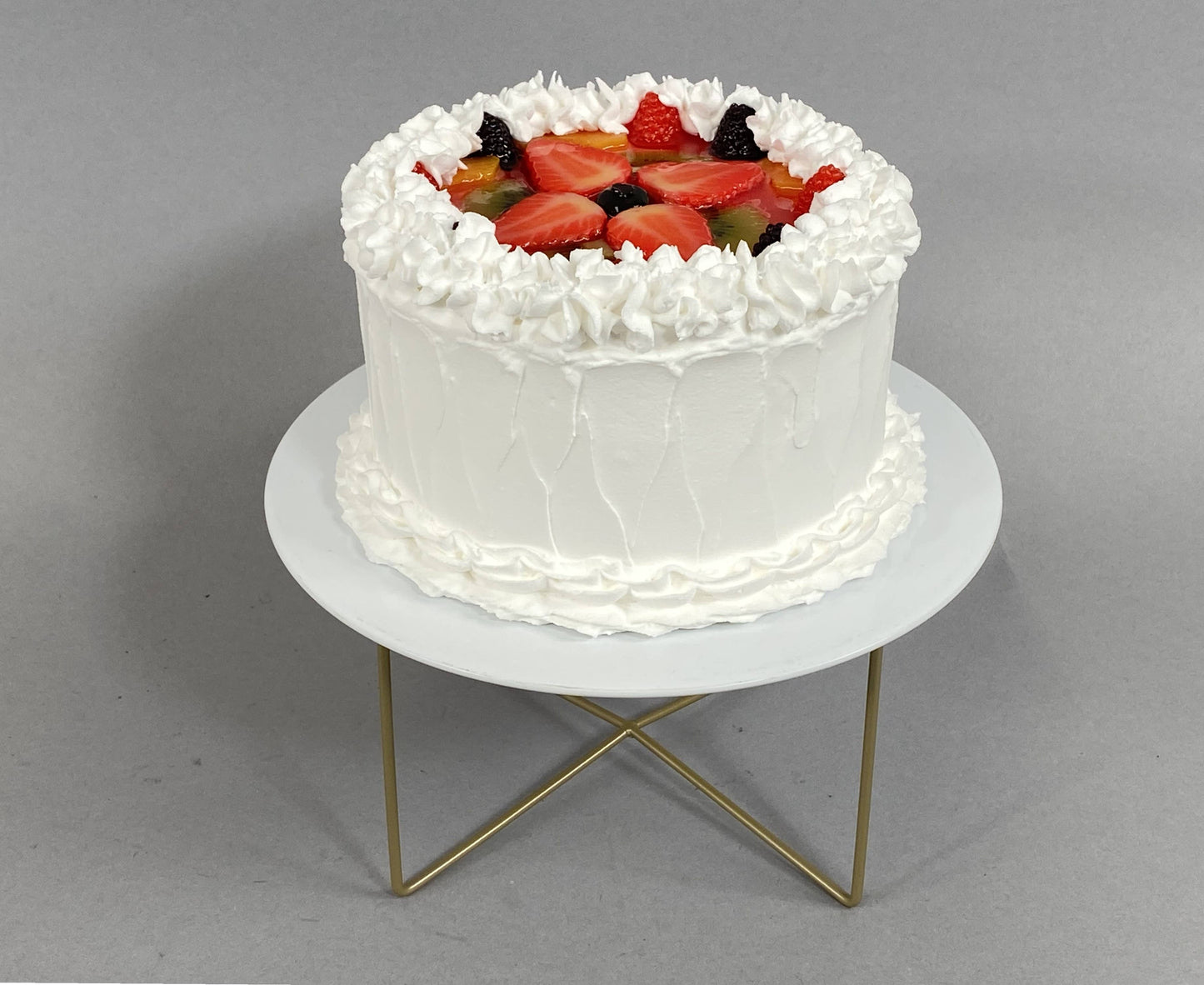 Small fake vanilla cake with white frosting and assorted fruits. Available size: small.