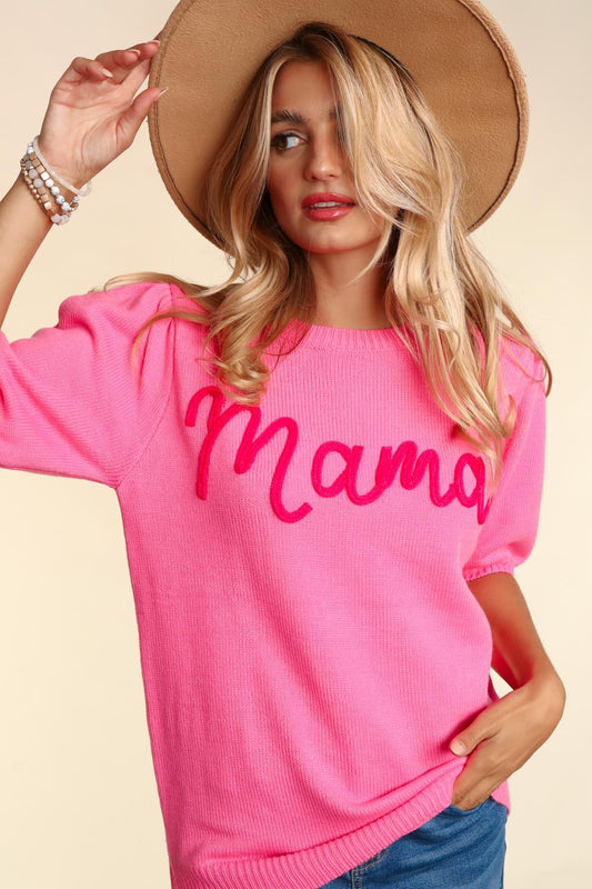 A woman in a pink Mama Embroidered Pop Letter Short Bubble Sleeve sweater, tipping a wide-brimmed hat, with a background in soft focus.