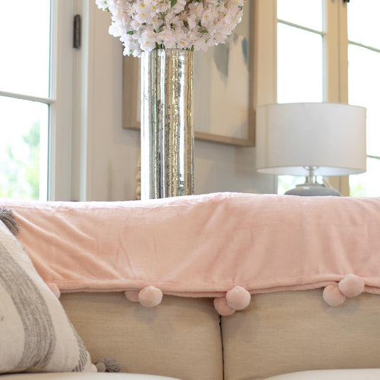 Light pink Cozy Pom Pom Throw, available in multiple sizes, features soft texture and playful pom poms.