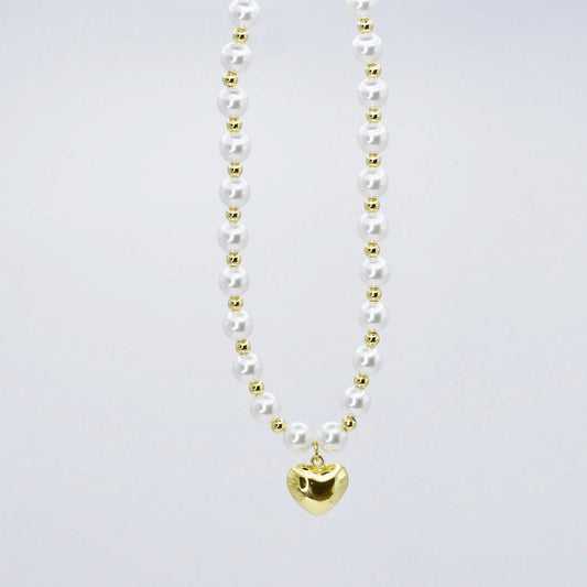 The Heart Pearl Necklace by Treasure Jewels features white pearls, gold beads, and a gold heart pendant. Available in various sizes.