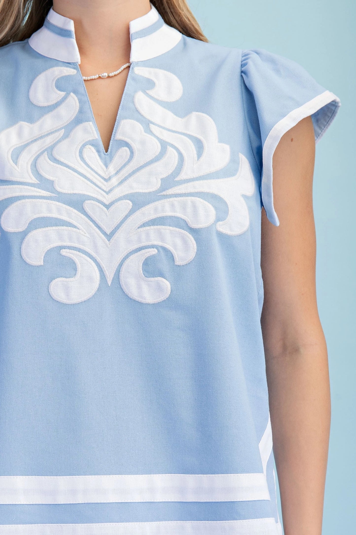 Light Blue Embroidered Appliqué Design Top with short ruffled sleeves, white chest appliqué. Sizes: XS–XL.