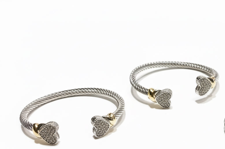 Two twisted silver heart bangles with gold accents and sparkling stone tips; available in small, medium, and large sizes.