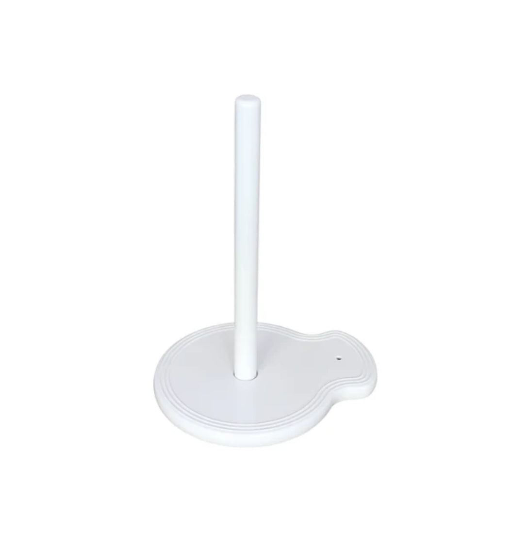 The "Paper Towel Holder Pinstripes" by nora fleming features a white design with a round base and a single vertical rod in the center. The base includes a small, curved extension on one side for added functionality and charm. Sizes available: N/A (one size fits all standard paper towel rolls).