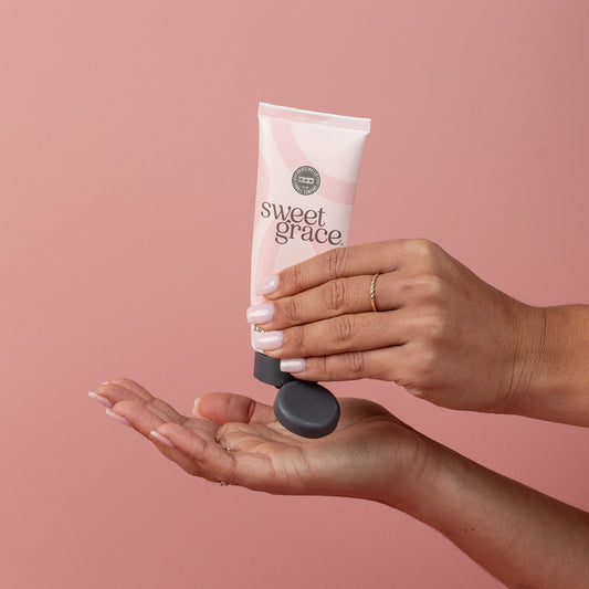 Sweet Grace Hand Cream being dispensed from a pink tube; available in 1.65 oz and 3 oz sizes.