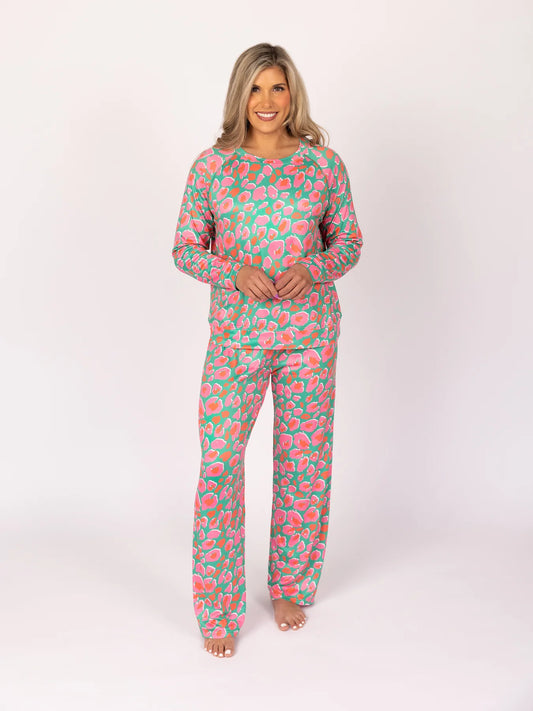 The Wild Child Annie pajama set features a colorful floral design in pink, green, and white hues. This cozy set includes a button-down long sleeve top and comfortable matching bottoms. Available sizes range from small to large.