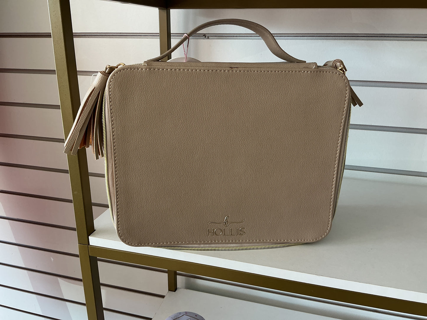 Tan rectangular Hollis Travel Make Up Bag with top handle, tassel zipper, and embossed logo on front; available in small, medium, and large sizes.