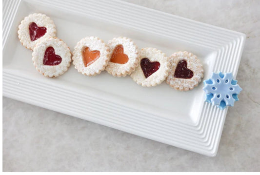 The Bread Tray Stripes: Rectangular white plate with a blue snowflake decoration, holding six cookies. Each cookie has a heart-shaped jam center (three red, three orange) and is dusted with powdered sugar. Available in sizes: Small, Medium, Large.