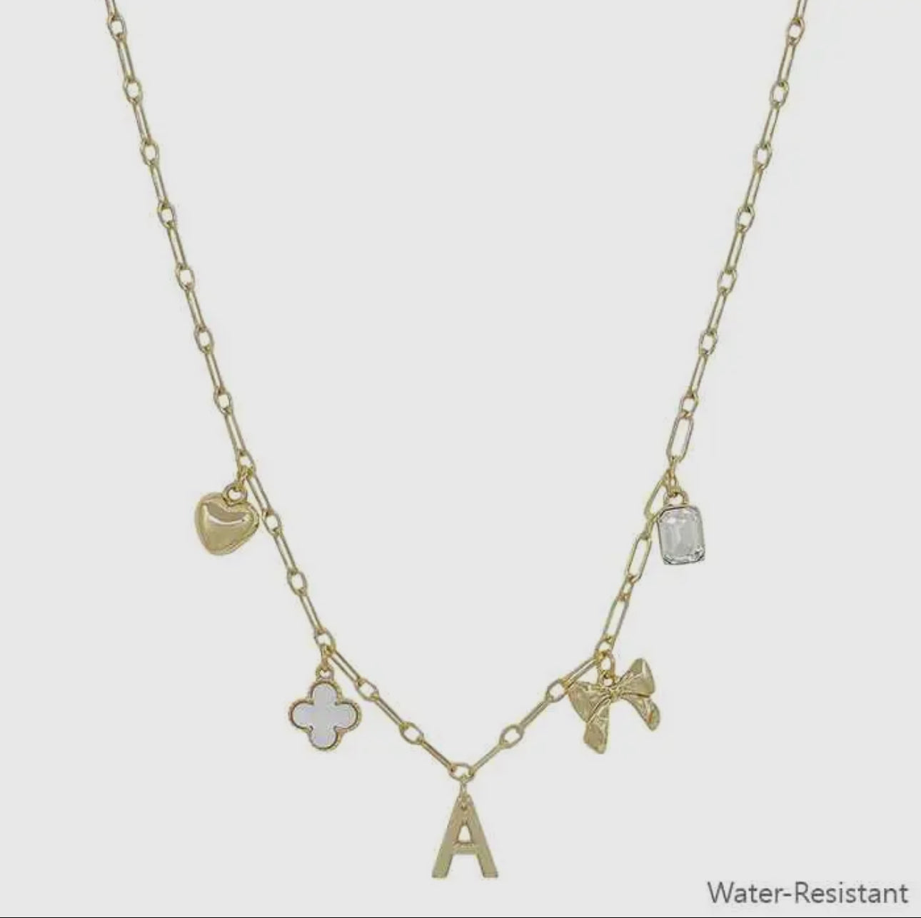 Water resistant gold chain necklace with five charms: heart, white clover, "A" initial, bow, and crystal. Sizes: S, M, L.