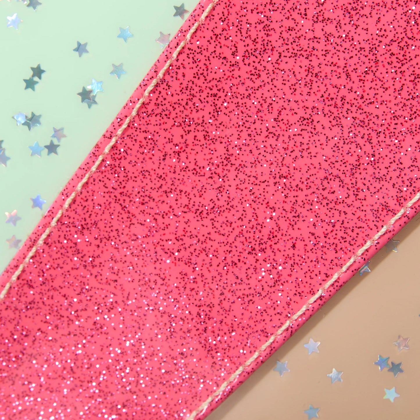 Uptown Crossbody in pink glitter with edge stitching, shown tilted. Available in small, medium, and large sizes.