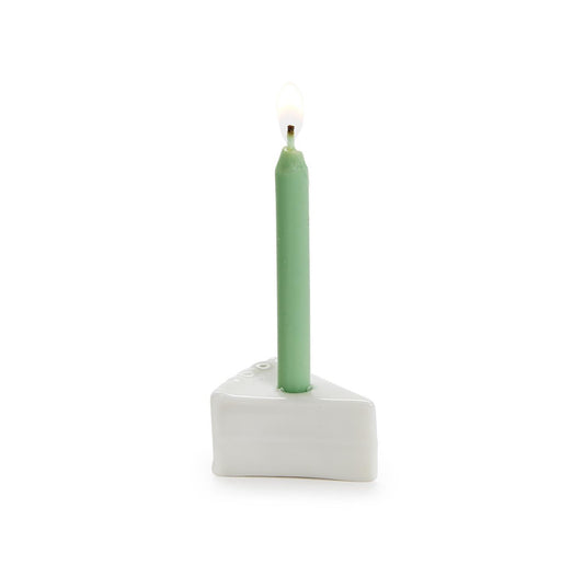 Lit green candle in a white, wedge-shaped porcelain cake slice holder. Available sizes: Small, Medium, Large.